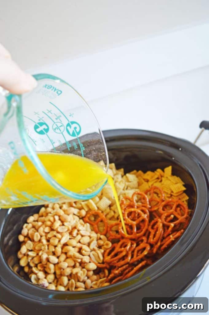 Irresistible Slow Cooker Chex Mix 5 Melted butter being poured over Chex cereal, pretzels, and peanuts in a crockpot.