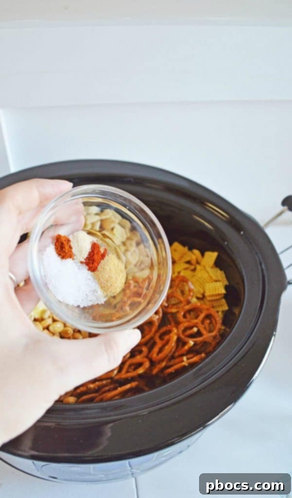 Irresistible Slow Cooker Chex Mix 6 Spices being sprinkled over the butter-coated Chex Mix in a slow cooker.