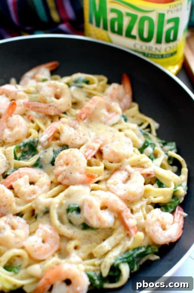 Fettuccine pasta being tossed with the creamy Cajun Alfredo sauce in a large skillet, ensuring even coating.