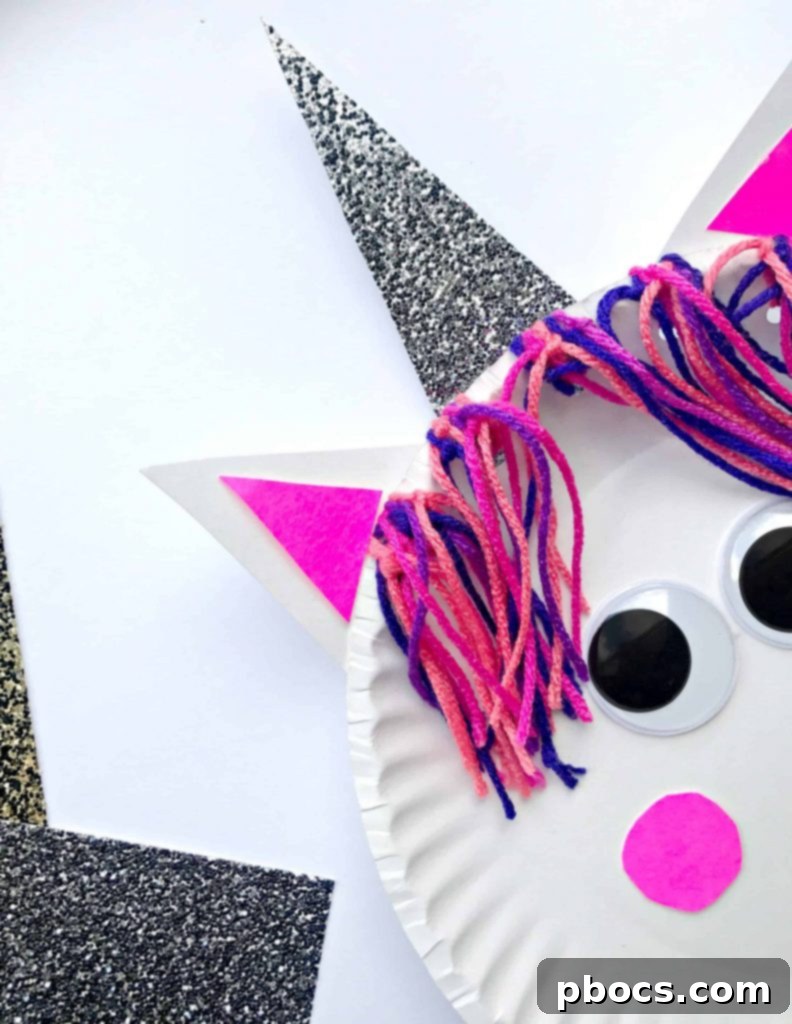 Two completed paper plate unicorn crafts, one with rainbow yarn, one with blue ombre yarn